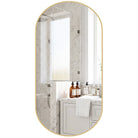 Front view of the gold oval pill-shaped metal frame mirror reflecting a marble bathroom