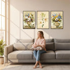 Set of three framed floral still-life prints above a gray sofa in a sunlit living room