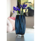 Blue-teal art glass vase with purple irises on a side table