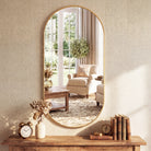 Oval pill-shaped metal frame mirror in gold above a wood console with books