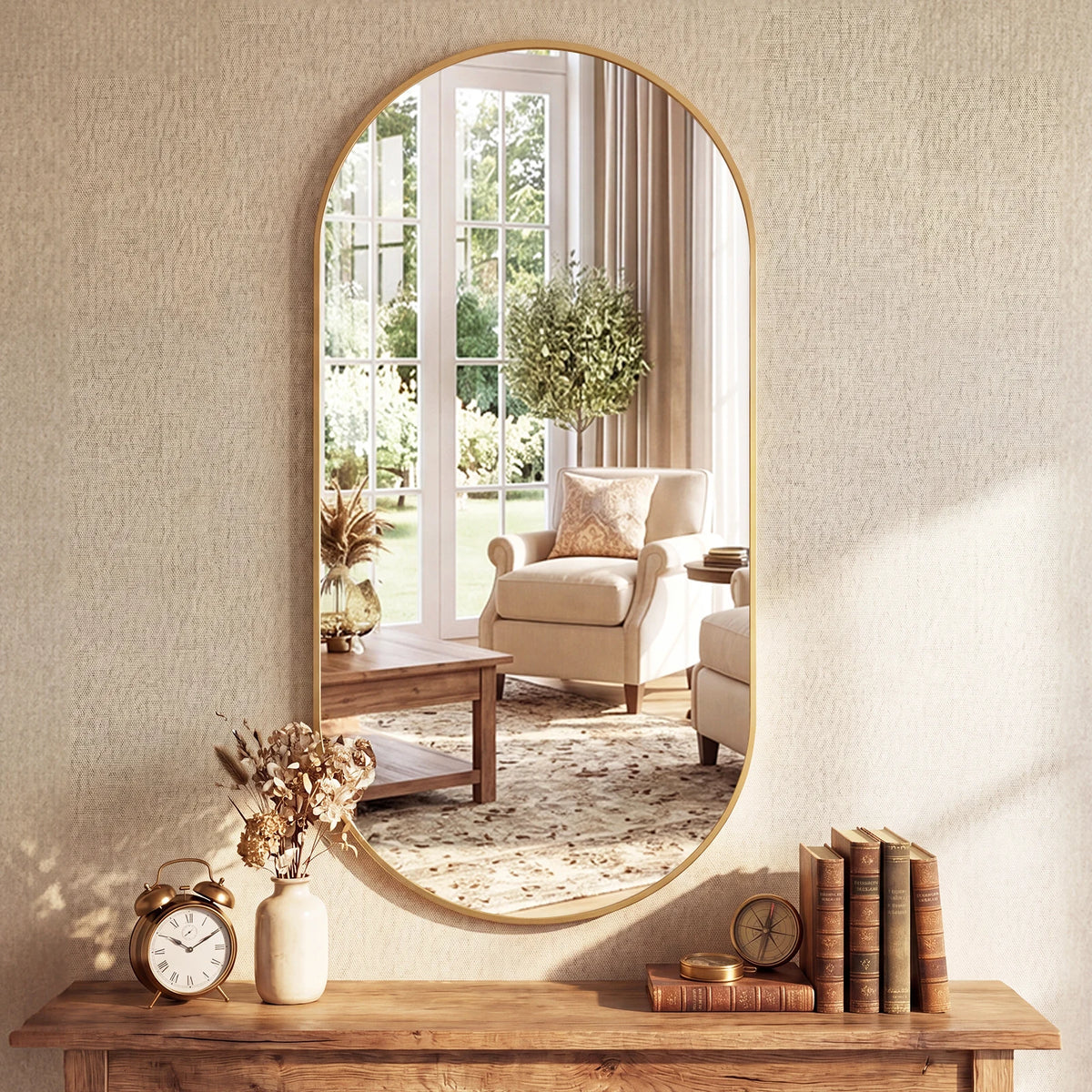 Oval pill-shaped metal frame mirror in gold above a wood console with books