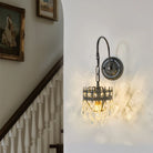 Crystal wall sconce with black iron arm illuminating a staircase wall beside framed art
