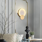 Round marble-look LED wall sconce with brass disc on a panelled wall