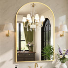 Arched gold metal frame bathroom vanity mirror between pleated sconces reflecting a crystal chandelier
