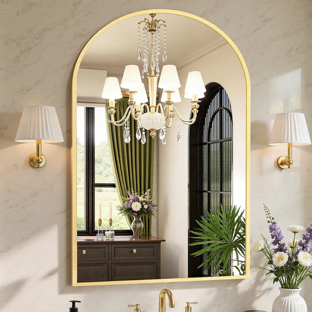 Arched gold metal frame bathroom vanity mirror between pleated sconces reflecting a crystal chandelier