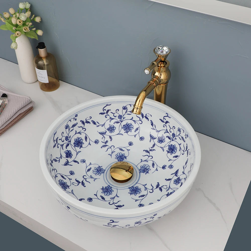 Hand-painted blue and white ceramic vessel sink with gold faucet and drain, seen from above