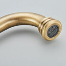 Close-up of the curved antique brass faucet spout end showing the mesh aerator