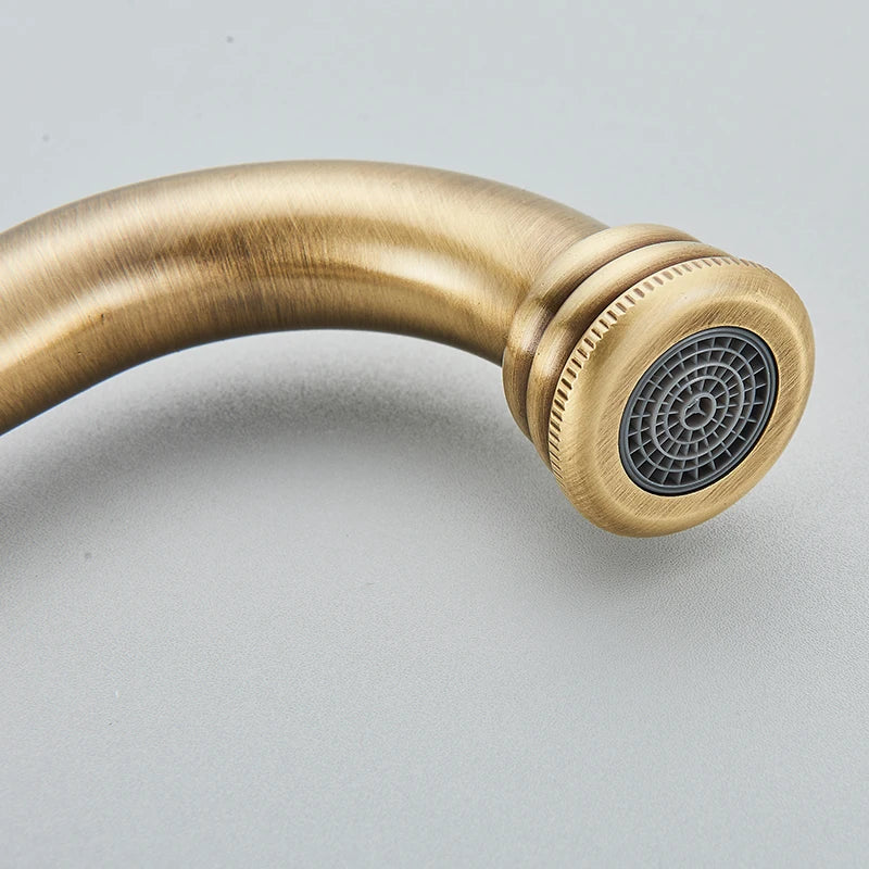 Close-up of the curved antique brass faucet spout end showing the mesh aerator