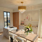 Gold fluted crystal chandelier glowing above a marble dining table and kitchen island
