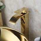 Close-up of the gold waterfall faucet spout above the polished gold vessel sink