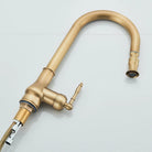 Angled view of the antique brass pull-out kitchen faucet showing gooseneck spout and supply hose