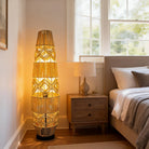 Tall woven cane rattan floor lamp glowing beside a bed