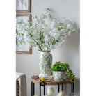 White and green floral ceramic vase with white blooms on a side table