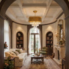 Gold fluted K9 crystal chandelier lit in a coffered-ceiling living room with arched shelves