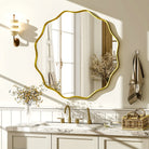 Scalloped round gold mirror reflecting a window above a white shaker bathroom vanity