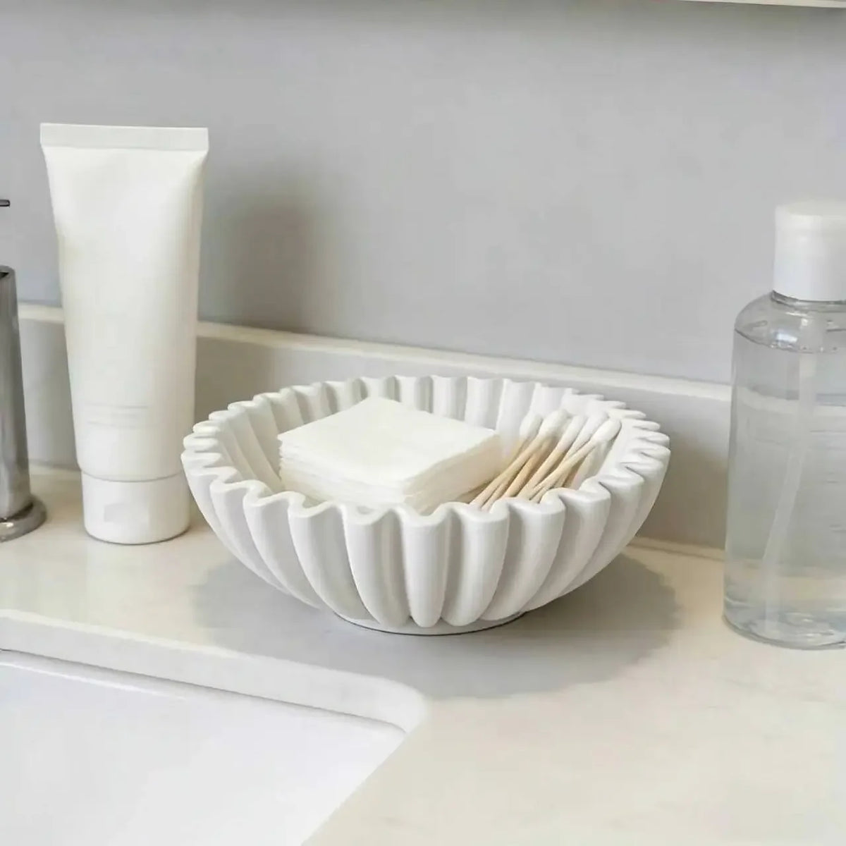 White pleated ceramic bowl with a scalloped rim holding small accessories
