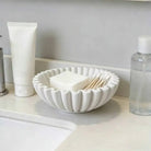White pleated ceramic bowl with a scalloped rim holding small accessories
