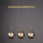 Three smoky grey glass globe pendants on a brass linear canopy