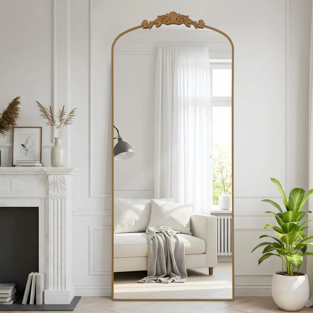 Arched gold standing floor mirror with carved crest leaning in a white living room