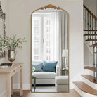 Ornate carved standing floor mirror with arched gold frame and crest beside a staircase