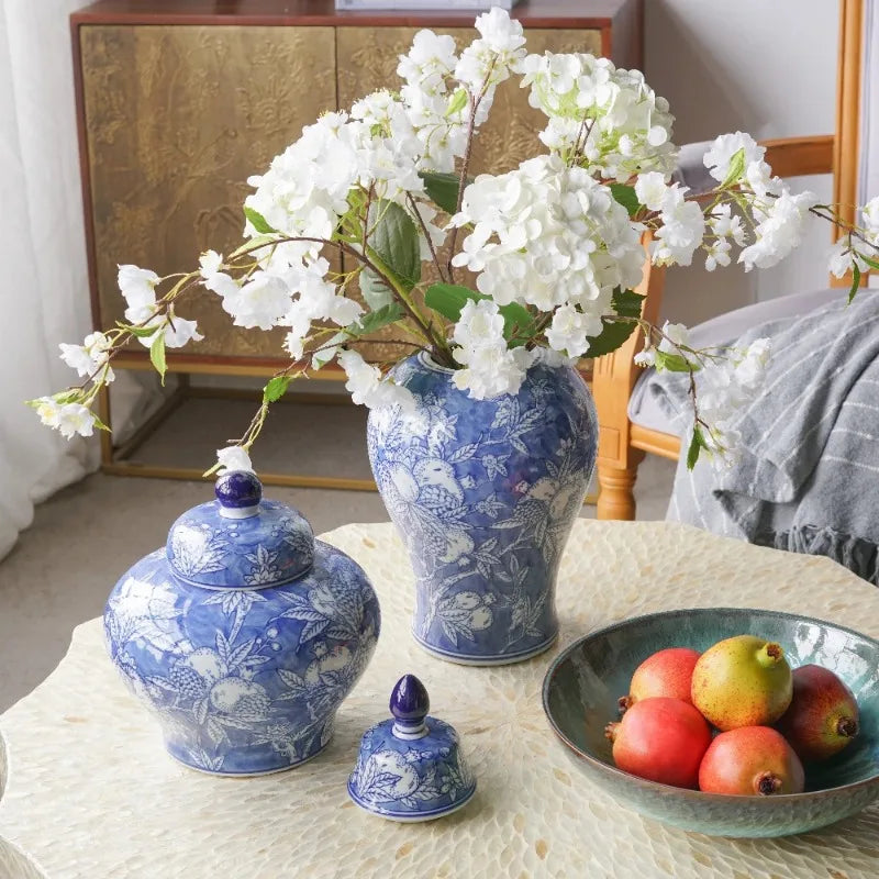 Blue and white lidded jar beside a matching vase with white blossoms