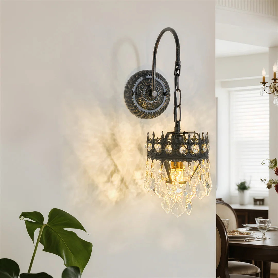 Crystal shade wall sconce on curved black iron arm glowing on a white wall