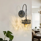 Crystal shade wall sconce on curved black iron arm glowing on a white wall