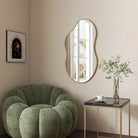 Organic gold-frame mirror above a side table beside a green lounge chair