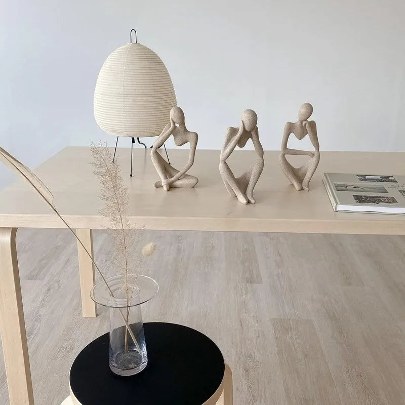 Three sandstone-finish thinker sculptures in different poses on a light wood desk