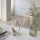 Seated sandstone-finish thinker figure sculpture with crossed legs on a white tabletop
