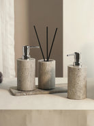 Two round gray travertine dispensers with silver-tone pumps and a reed diffuser holder
