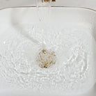 Close-up of the glossy white ceramic basin, gold rim and matching gold drain