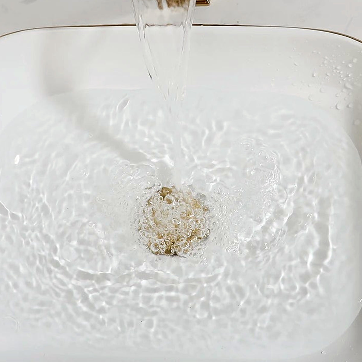 Close-up of the glossy white ceramic basin, gold rim and matching gold drain