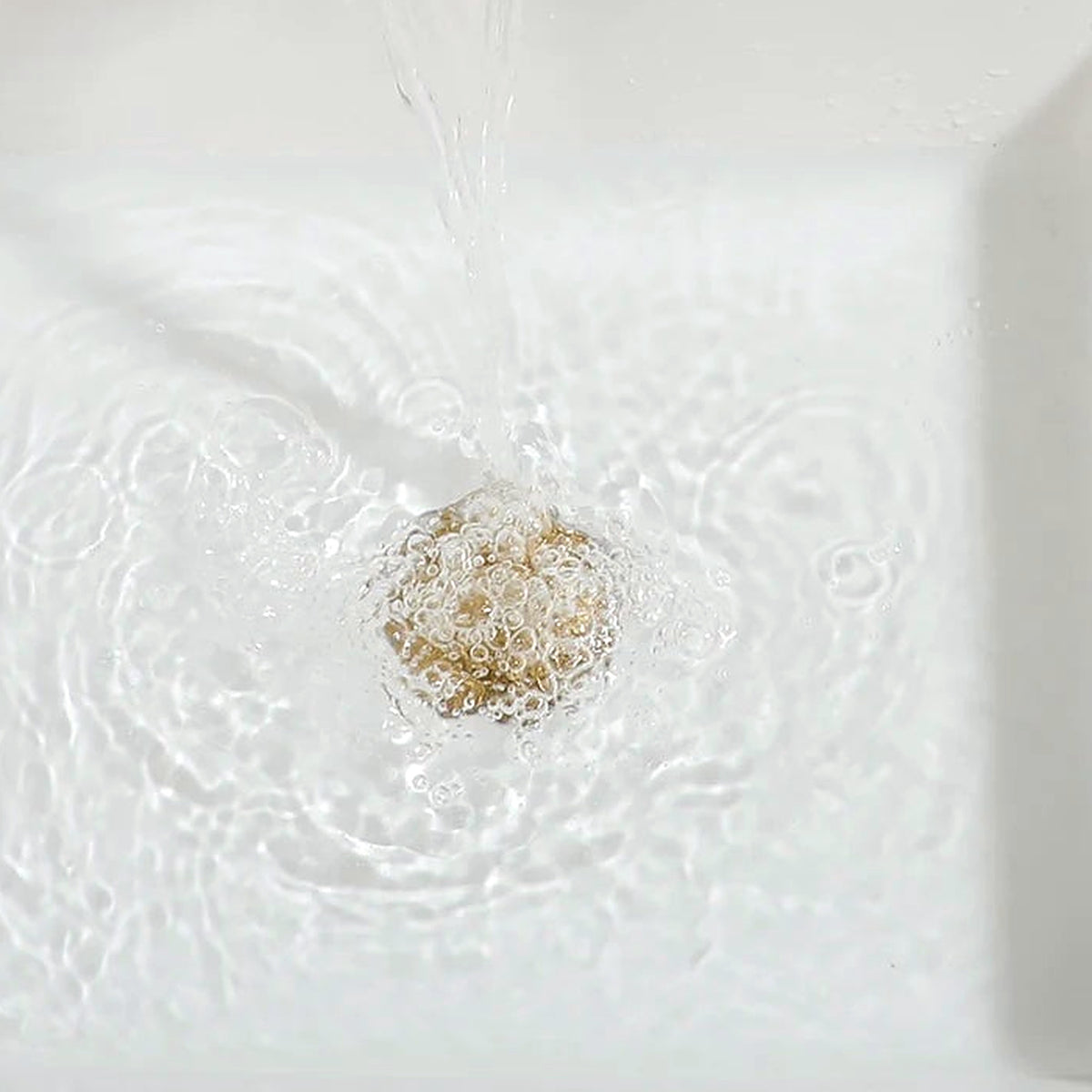 Close-up of the white ceramic basin and gold rim with running water
