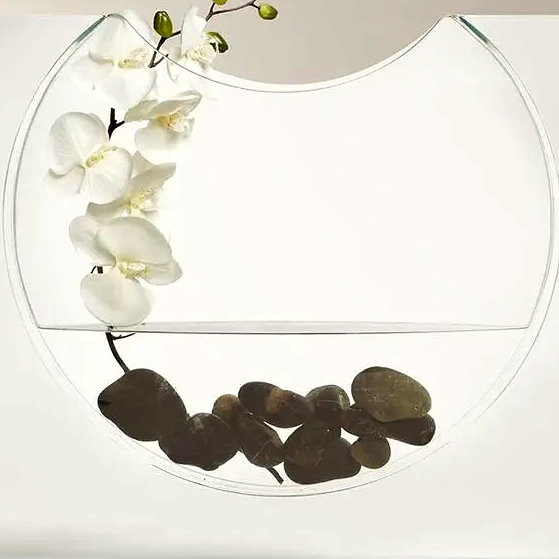 Close-up of the clear ellipse vessel holding orchid stems and dark river stones