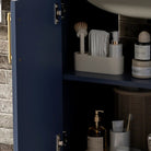 Detail of the open navy cabinet door, hinge and satin gold pull (toiletries shown for styling)