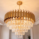 Gold five-tier raindrop crystal chandelier glowing against a soft neutral wall