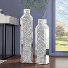 Pair of mirrored crushed-crystal floor vases, 24 and 30 in, glittering beside a sunlit window
