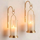 Pair of gold hurricane candle wall sconces with clear glass shades glowing with pillar candles (candles not included)
