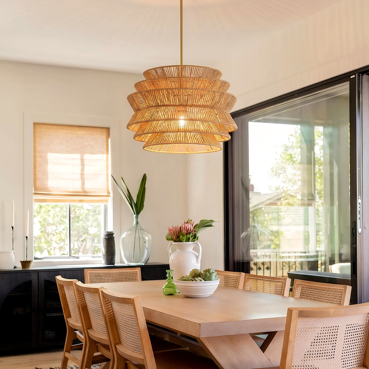 Hand-woven tiered pendant light glowing above a light wood dining table (furniture and décor shown for styling)