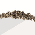 Ornate floral rose crest in antique brass crowning the arched mantel mirror