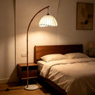 Bamboo arc floor lamp casting warm light beside a bed (bedding and décor shown for styling; bulb shown for illustration)