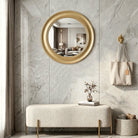 Brushed gold round wall mirror in an entryway above a cream bench (furniture and décor shown for styling)