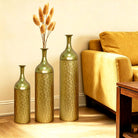 Set of three gold leaf-pattern floor vases beside a sofa (furniture and dried botanicals shown for styling)