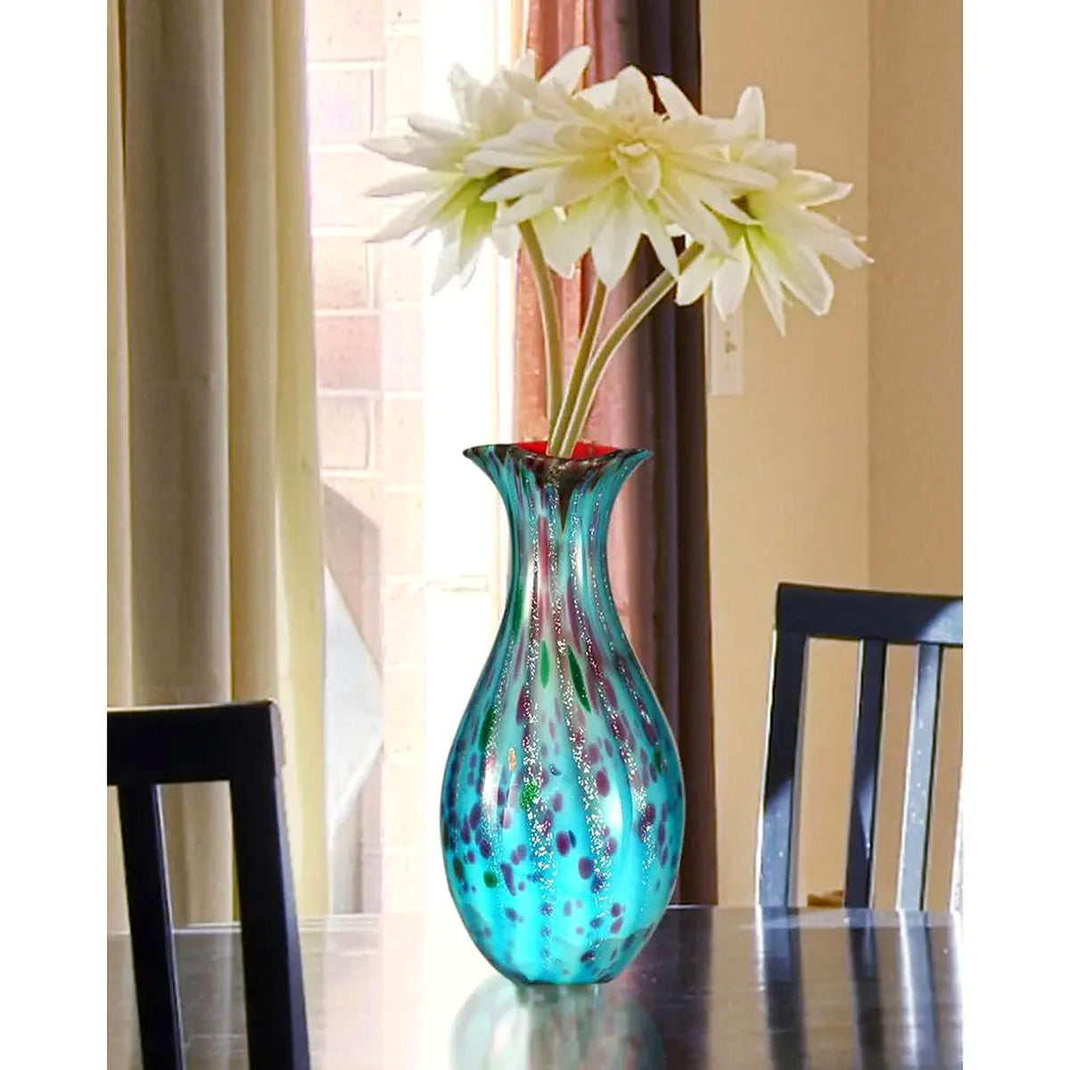 Hand-blown teal art glass vase on a dining table with white star-shaped blooms (flowers and furniture shown for styling)