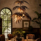 Tiered bronze palm fronds of the pendant chandelier against a textured wall with palm artwork (art shown for styling)