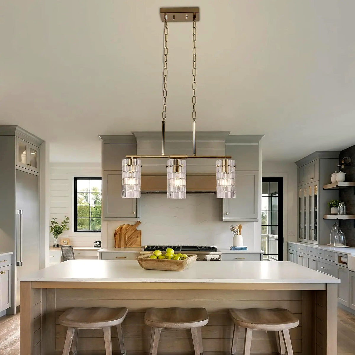 Brass three-light linear pendant over a kitchen island (cabinetry and décor shown for styling)