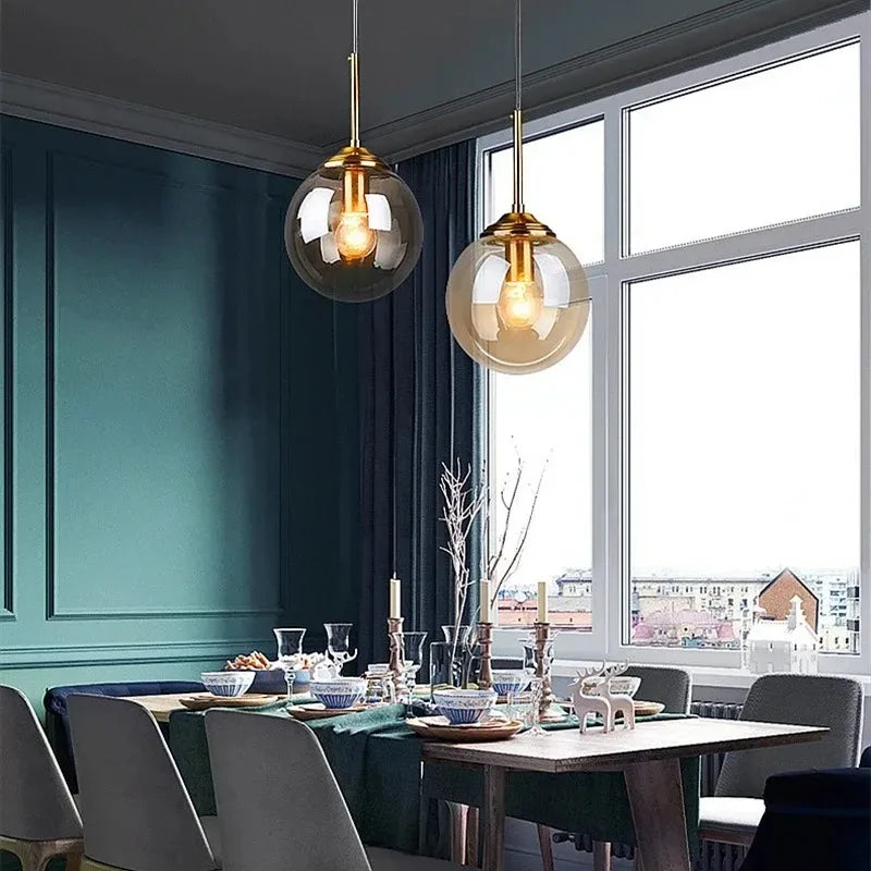 Amber and clear glass globe pendants with brass stems glowing by a window