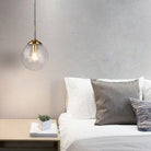 Clear glass globe pendant light glowing beside a bed