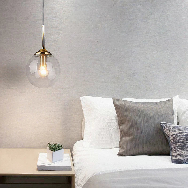 Clear glass globe pendant light glowing beside a bed